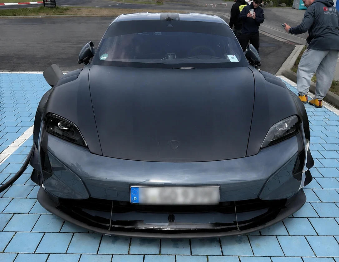 Frontansicht des rekordverdächtigen Porsche Taycan mit angeschlossenem Ladekabel und dem Porsche-Emblem auf der Motorhaube.