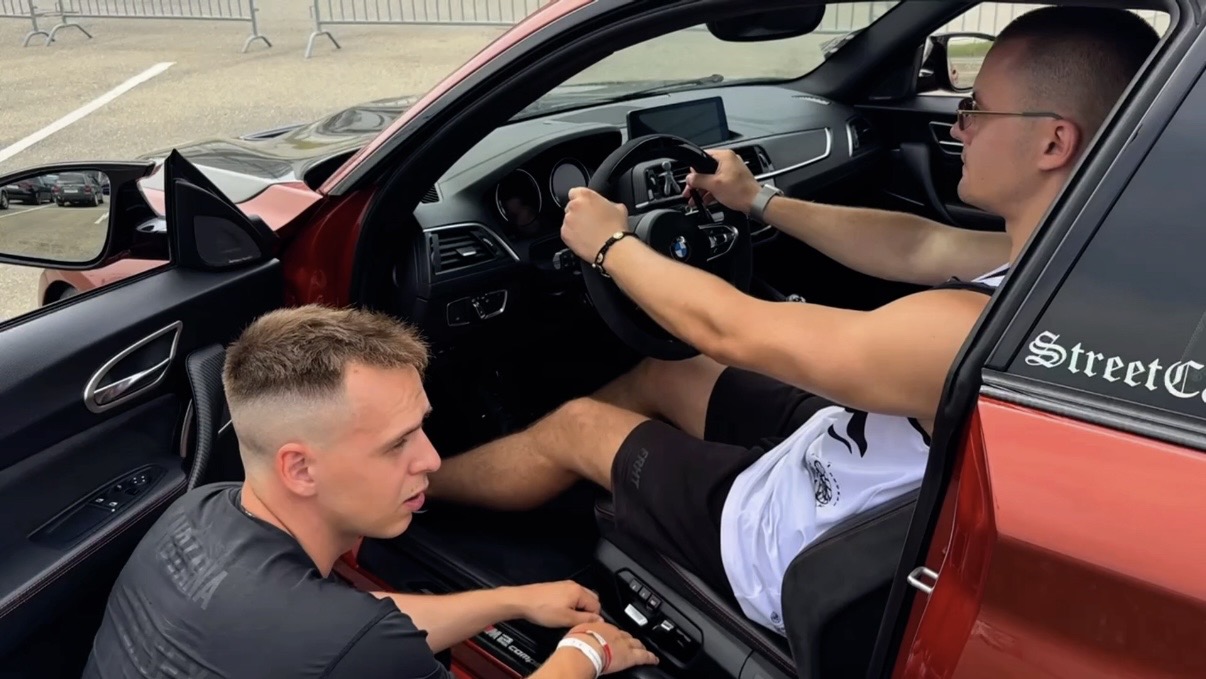 Ein Rennfahrlehrer erklärt einem Schüler den richtigen Griff am Lenkrad und die richtige Sitzhaltung am Steuer eines BMW