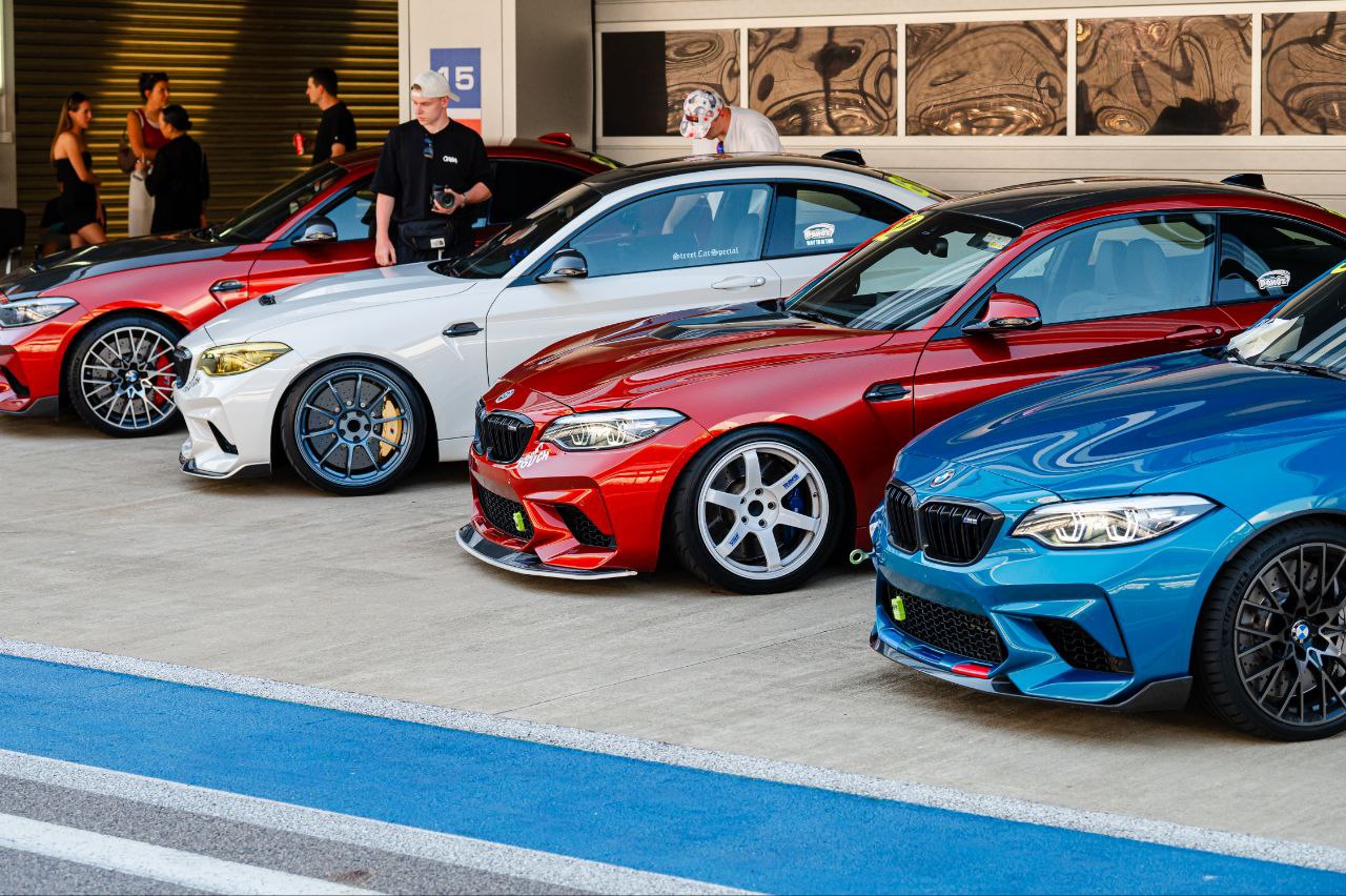 Vier tiefergelegte BMW M2 in verschiedenen Farben stehen in einer Reihe vor den Boxen vor dem Track-Day, im Hintergrund unterhalten sich die Fahrer und Instruktoren