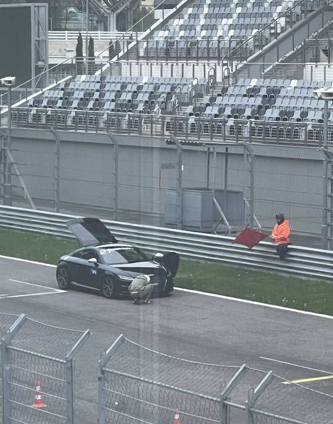 Ein Auto, dessen Motor am Straßenrand ausgegangen ist, im Hintergrund ein Streckenposten mit einer roten Flagge.