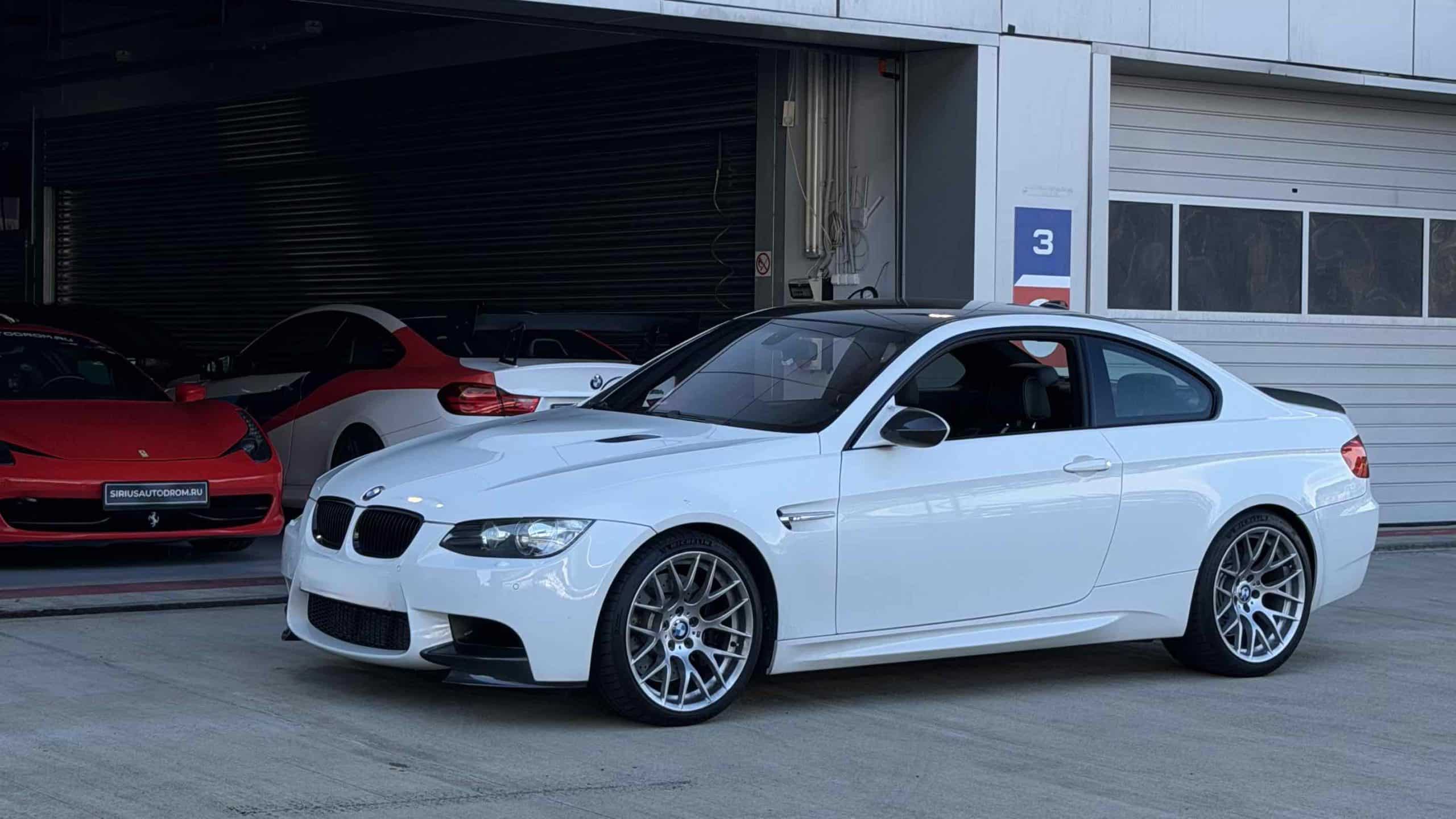 Ein weißer BMW M3 E92 mit Originalfelgen des Modells Style 359M, der auf der Pit Lane gekauft wurde, sowie ein Ferzi 458 hinten und ein BMW M4