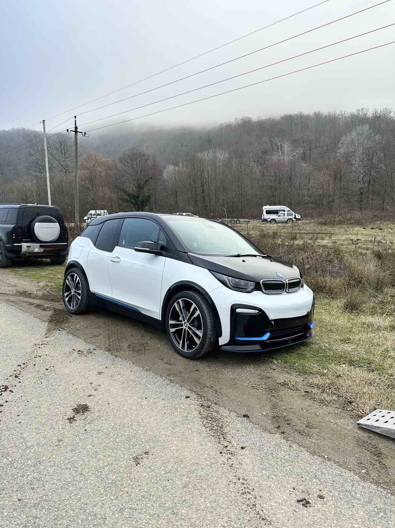 Der BMW i3S steht am Straßenrand vor dem Hintergrund eines Waldes – Ansicht von vorne und von der Seite.