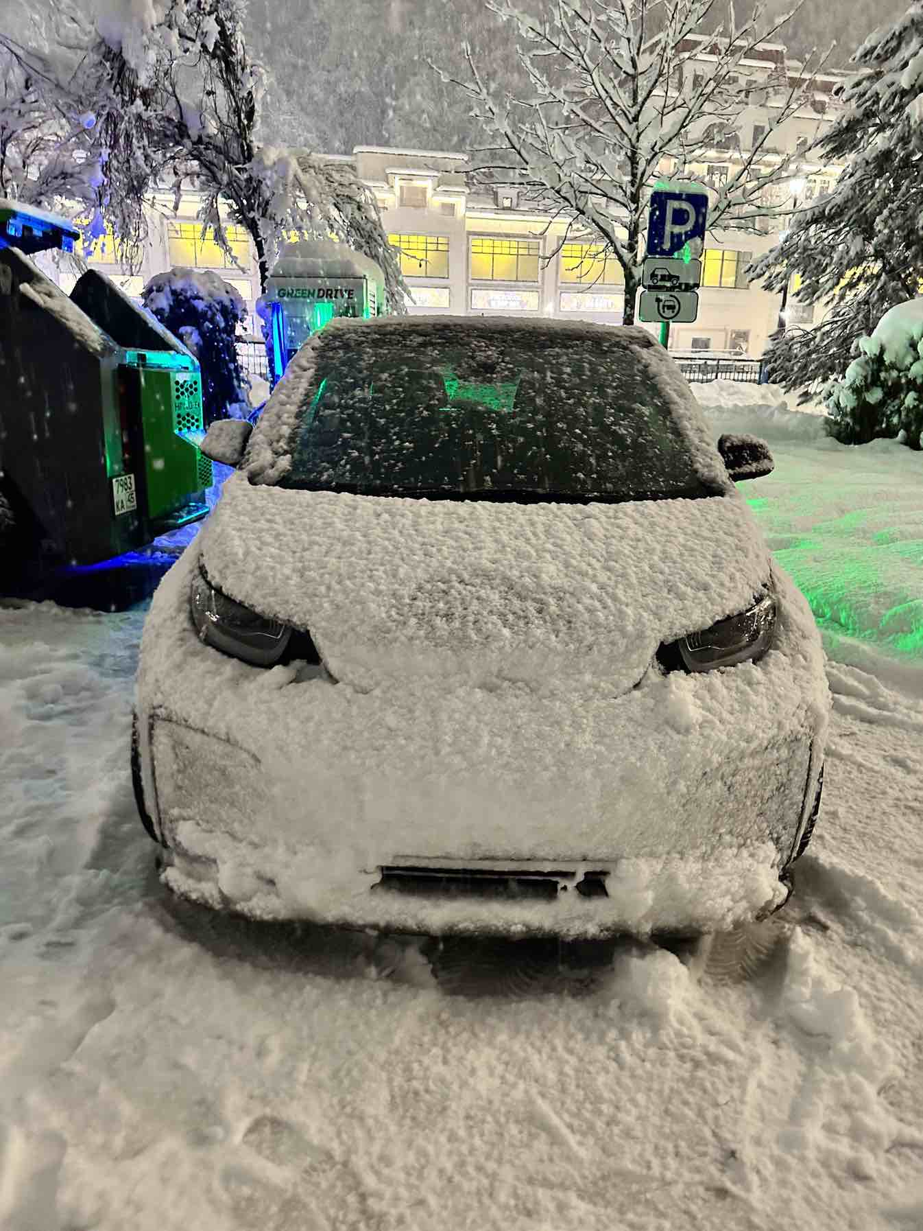 Ein komplett mit Schnee bedeckter BMW i3S steht während eines heftigen Schneefalls auf einem Parkplatz.